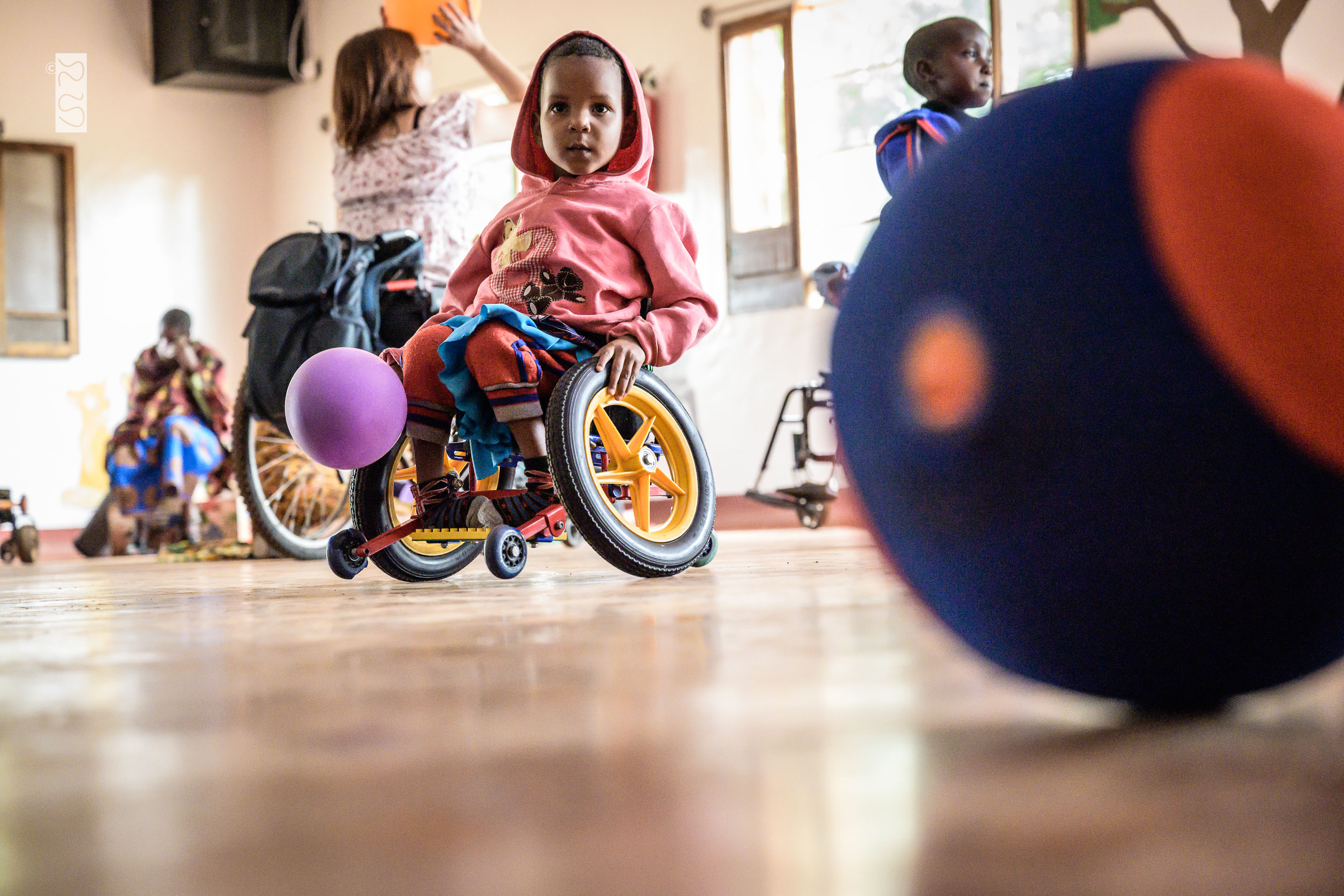 Lek och rörelse: barn i liten färgglad rullstol med människor i rörelse i bakgrunden